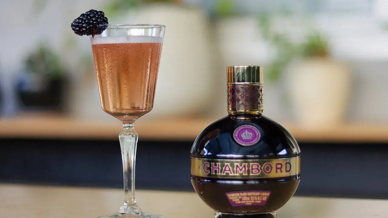 Elegancki kieliszek z różowym drinkiem i jeżyną obok butelki likieru Chambord.