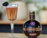 Elegancki kieliszek z różowym drinkiem i jeżyną obok butelki likieru Chambord.