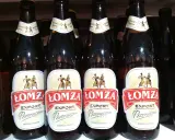 Butelki piwa Łomża Export Pszeniczne w rzędzie. Etykiety z postaciami i kłosem zboża.