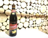 Butelka piwa Litovel Černý Citron na tle drewnianej ściany z plastrów drewna.