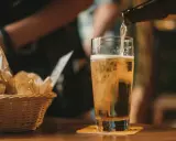 Z butelki leje się złociste piwo IPA do szklanki. Obok koszyk z pieczywem.