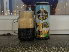 Perlenbacher Schwarz Bier w kuflu, obok puszka piwa. Wieczorny widok na miasto w tle.