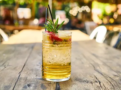 Orzeźwiający drink z wódką waniliową, lodem, owocami i gałązką rozmarynu na drewnianym stole.
