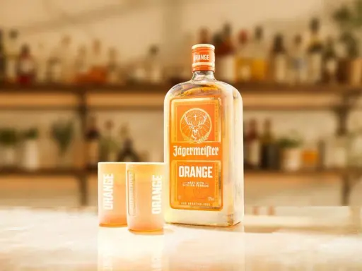 Butelka Jägermeister Orange i dwa kieliszki z napisem "ORANGE" na blacie. Idealny zestaw na letnie wieczory.
