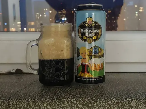 Perlenbacher Schwarz Bier w kuflu, obok puszka piwa. Wieczorny widok na miasto w tle.
