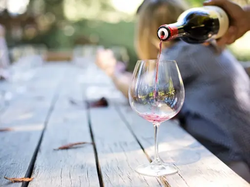Czerwone wino nalewane z butelki do kieliszka na drewnianym stole.