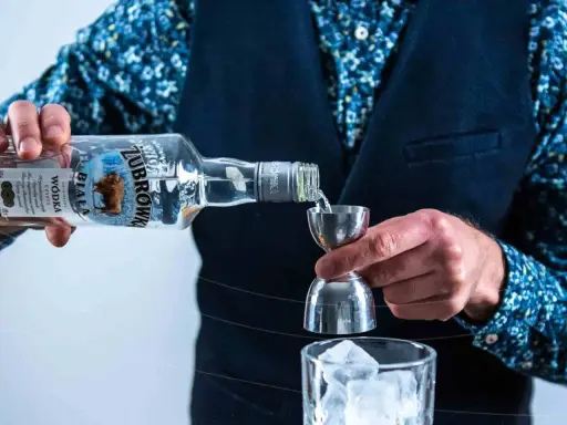 Barman nalewa Żubrówkę do jiggera, przygotowując drinka. W tle szklanka z lodem. Wataha wodka w butelce.