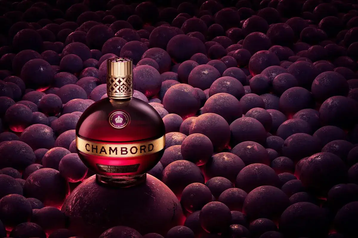 Elegancka butelka likieru Chambord wśród ciemnych, okrągłych owoców.