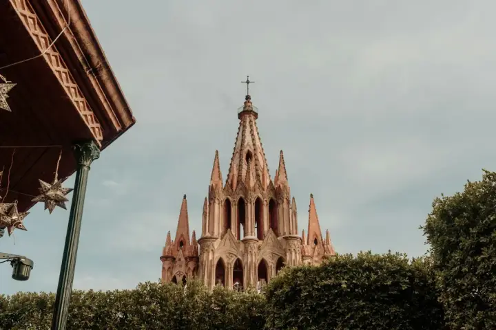 Imponująca iglica kościoła w San Miguel, otoczona zielenią, z ozdobnymi gwiazdami zwisającymi z zadaszenia.